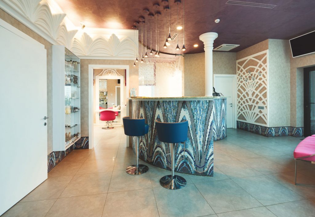 Modern reception interior. Front desk of beauty or spa salon. Entrance hall with tiled counter, comfortable chairs and couch, copy space on white door